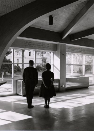 <p>Unidentified individuals standing in the Memorial Union Commons, ca. 1960s. The wall that they face reads "I believe in Oregon State and in her democracy and her far reaching bond of beaver brotherhood. <span class='highlight1 bold'>I</span> believe in Oregon</p><p>				State - and since she has accepted me as a beaver <span class='highlight1 bold'>I</span> too am a guardian of beaver spirit."</p>