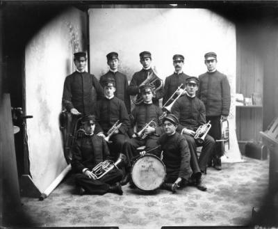 The OAC Band, ca. 1899, posing with the Corvallis High School drum. The drum is illustrated with a drawing of the Battleship Oregon.