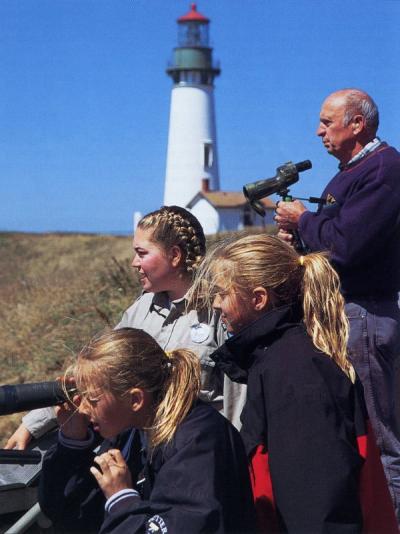 Image from an article titled "Job Shadows" describing internship positions that OSU Fish and Wildlife majors have completed as part of their degree requirement. Caption reads: "Nemesia Herzstein (center) points out sea life to visitors at the Yaquina Head Lighthouse and Interpretive Center. Herzstein interned with the Bureau of Land Management as a naturalist."