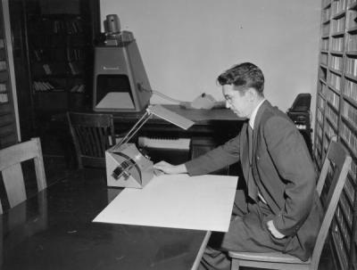 Rodney Waldron, seated with the new portable microfilm reader, December 1958.