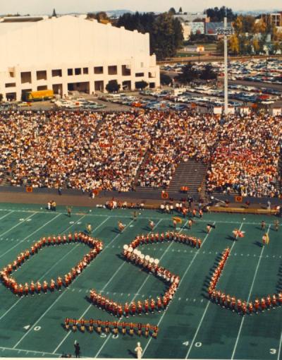 The OSU Marching Band performing at halftime of the OSU-UCLA football game at Parker Stadium, 1972. Gill Coliseum is seen in the background.