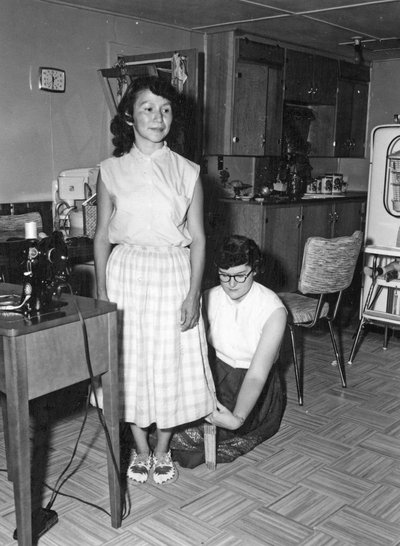 Mary Anne Crocker measures the hem of a skirt for a young homemaker on the Warm Springs Indian Reservation” 