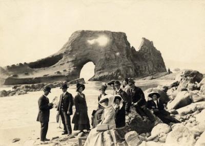 College students on Nye Beach in Newport, Oregon, May 1910. The woman in black sitting on the rock at front of photo is Ethel Allen. Ruby Elliott is the woman seen between the two men at the back of the group of students.