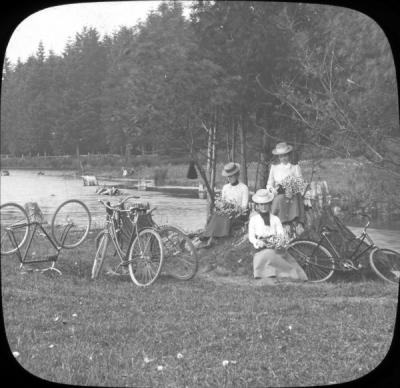 Women bicyclists sitting with flower bouquets, circa early 1900s.