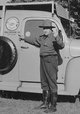 Conservationist Bill Schaeffer pointing to the Oregon Wildlife Federation emblem on the OWF public relations car, ca. 1960.