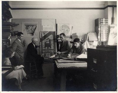 Black and white photograph of Roger Hayward examining blueprints.