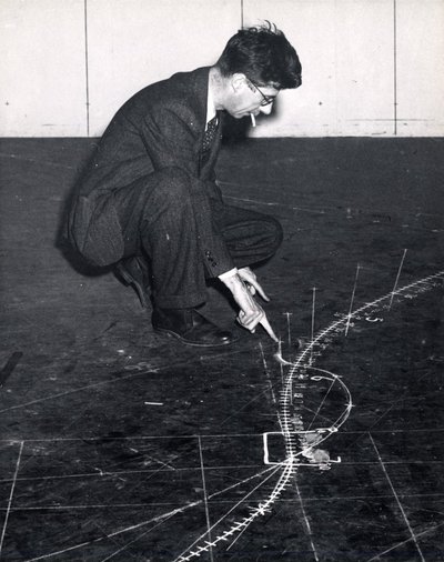 Black and white photograph of Roger Hayward tracing a trajectory on the floor.